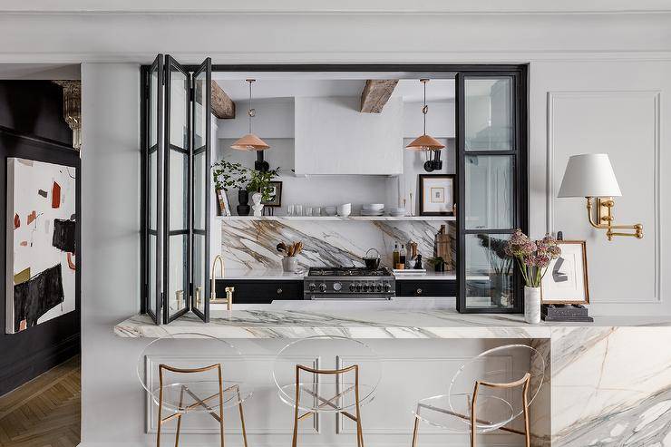 Kitchen passthrough with black folding doors, marble bar and brass and lucite round back barstools are featured in this transitional dining room.