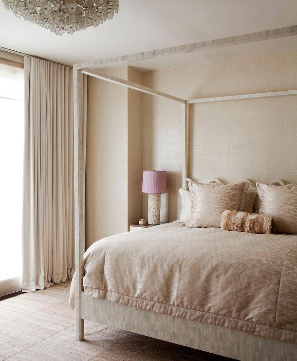 Elegant bedroom features a cream capiz canopy bed placed against a cream wallpapered wall lit by a cream lamp with a pink pleated lamp shade.