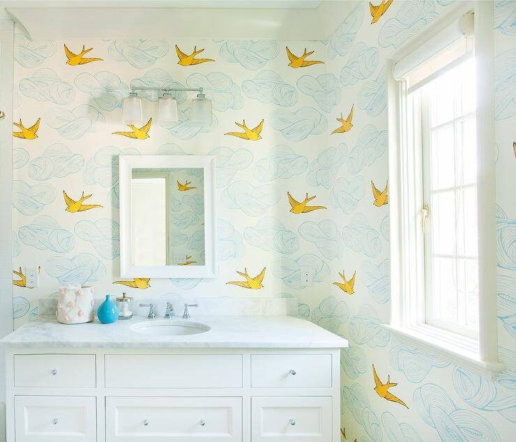 bathroom features blue and yellow wallpaper with cloud like shapes and flying birds, white vanity cabinet with nickel knobs and white marble countertop