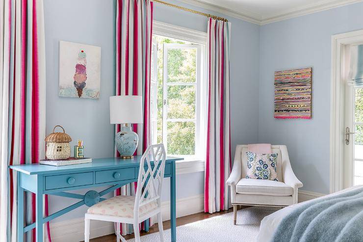 white bamboo chair sits at a turquoise blue desk topped with a blue chinoiserie lamp and placed beneath an ice cream art piece hung from a blue painted wall