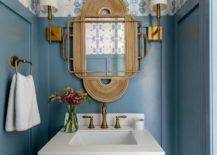 blue wall with wallpaper gold mirror wall sconces in half bathroom with white sink towel rack
