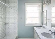 A pair of vintage glass birdcage chandelier hang over a double bath vanity topped with honed gray marble fitted with his and hers sinks placed under metal framed mirrors. A marble diamond pattern floor leads to a drop-in tub clad in white subway tiles finished with dark grout.