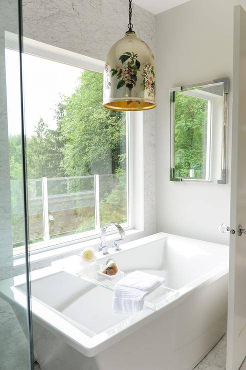 Master bathroom features a modern freestanding tub accented with a lucite tray and a deck mount gooseneck tub filler placed under a picture window illuminated by a bold pendant.