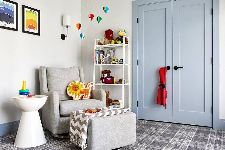 Transitional gray boy's nursery features powder blue double closet doors with black handles, white toy shelf, gray wingback nursery glider, nursery hot air balloons mobile and gray plaid carpeting.