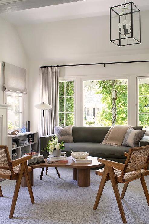 Light gray curtains cover windows located behind a dark gray sofa matched with a kidney shaped coffee table placed on a light gray rug in front of mid-century modern cane chairs.