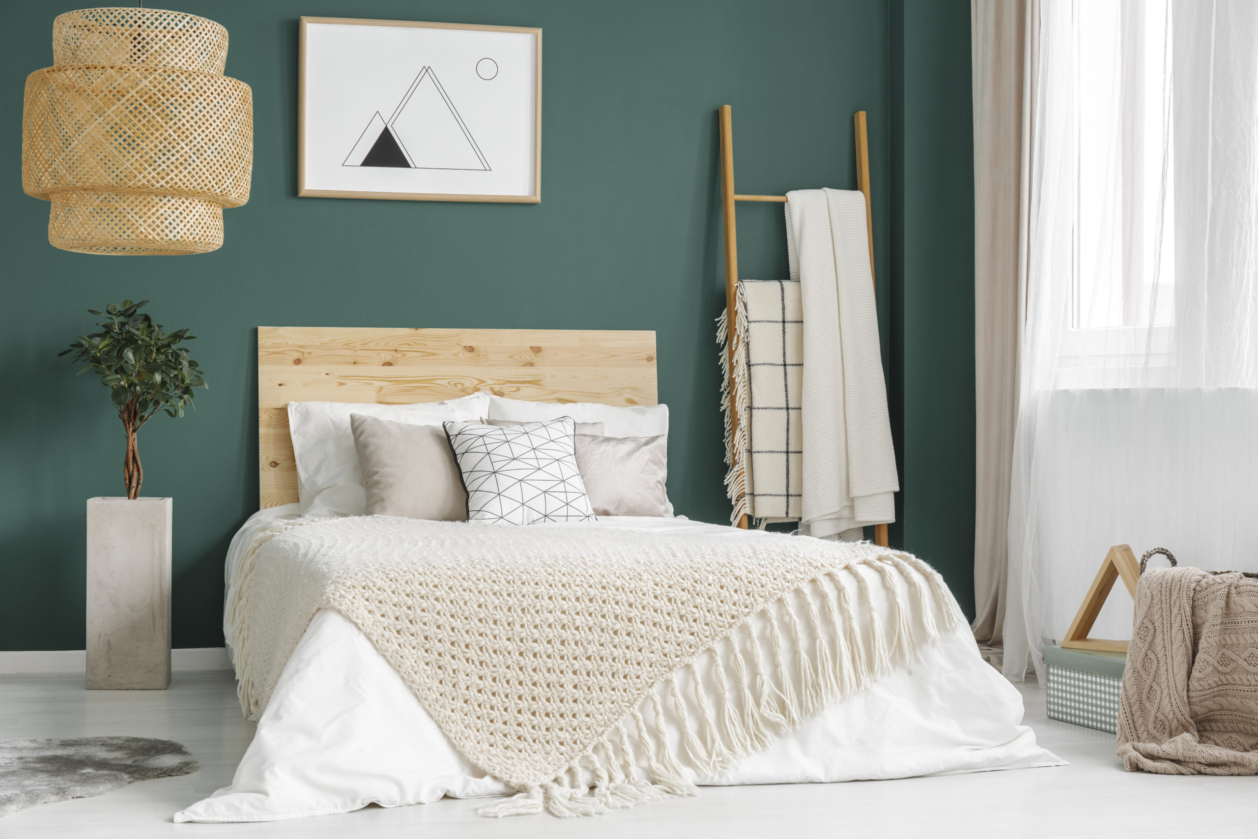 Plant and rattan lamp in green cozy bedroom interior with wooden bed against the wall with poster