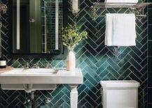 Bathroom features a white pedestal sink on a green herringbone pattern tiled wall, a black framed medicine cabinet, a nickel train towel rack over the toilet and white and gray diamond floor tiles.