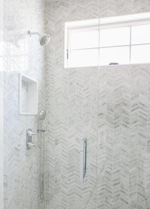 Walk in shower features gray marble chevron tiles, a tiled shower niche, a nickel shower kit and a clear partition.