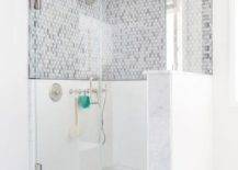 White marble floors topped with a gray trellis bath mat lead to a frameless glass door opening to a walk in marble and glass steam shower fitted with a tilt out window, mosaic marble floors, and gray oval marble tile backsplash holding a polished nickel shower kit and circular shower head while the ceiling holds a rain shower head in this well appointed contemporary bathroom.