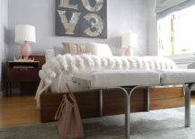 Fantastic bedroom with love art over wood platform bed dressed with Moroccan wedding blanket with wide headboard flanked by pink lamps on mid-century modern nightstands as well as mid-century modern bench at foot of bed over gray rug.
