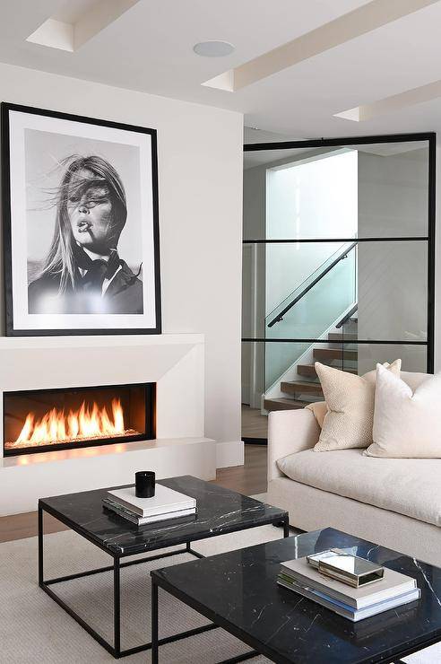 Living room features black and white art mounted over a modern beveled fireplace, an ivory sofa, and side-by-side black marble frame coffee tables.