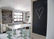 Spacious kitchen features a light taupe kitchen bar with custom beer tap and mini beverage fridge, light taupe cabinets with white shelves, glossy mint green stools at a glossy white lacquer freestanding kitchen island atop a light gray rug, and a built in chalkboard.
