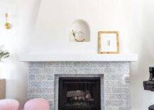 Pink stools sit in front of a vintage white and gray mosaic tiled fireplace positioned beneath a small arched niche.