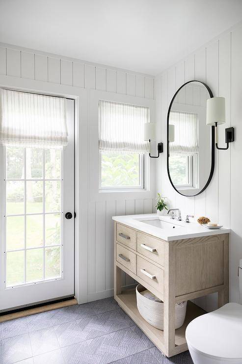 Black chevron floor tiles complement a powder room boasting a black oblong mirror hung between oil rubbed bronze sconces mounted to vertical shiplap trim above a beige limed oak washstand.