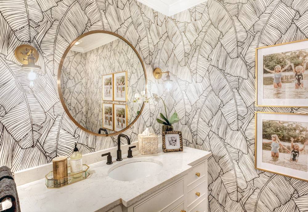 black and white leaf print patterned wallpaper in bathroom with white cabinet and gold accents