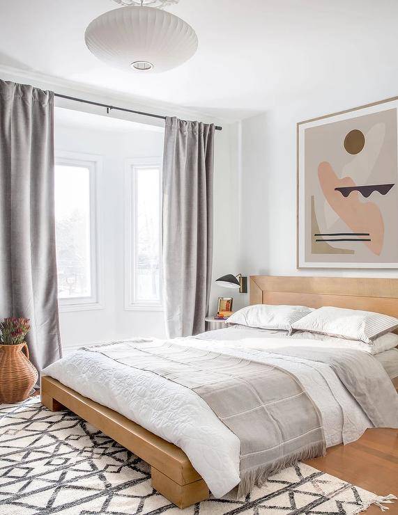 tan wood bed with abstract art hanging above grey curtains white walls bedroom