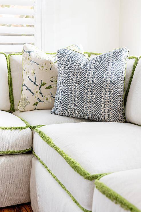 White sectional boasts green fringe trim and blue and white accent pillows.