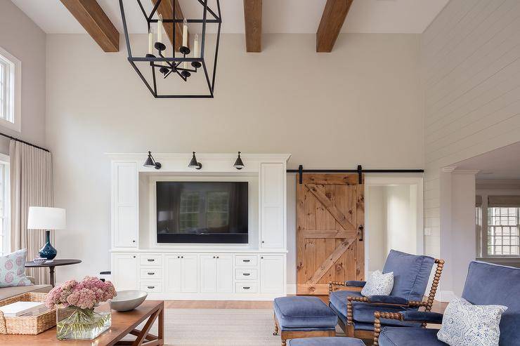 Family room with a barn door on rails encloses a space with a built-in entertainment center, a set of barn sconces and a set of blue pillow top spindle chairs with matching ottomans.