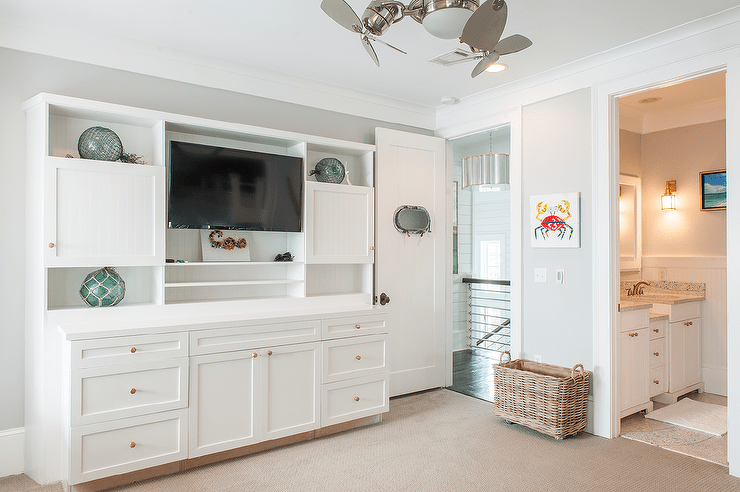 A vintage ceiling fan lights a cottage style family room boasting a white entertainment center accented with beadboard trim and brass hexagon knobs.