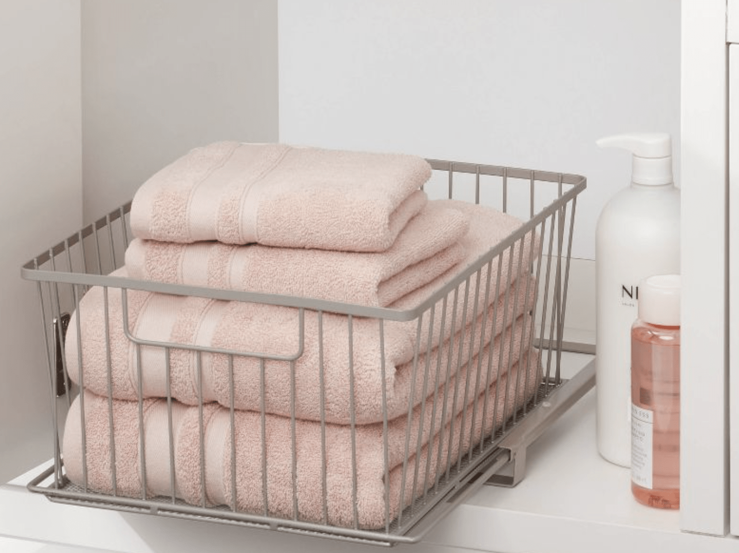 pink towels folded in open drawer inside bathroom closet next to shampoo